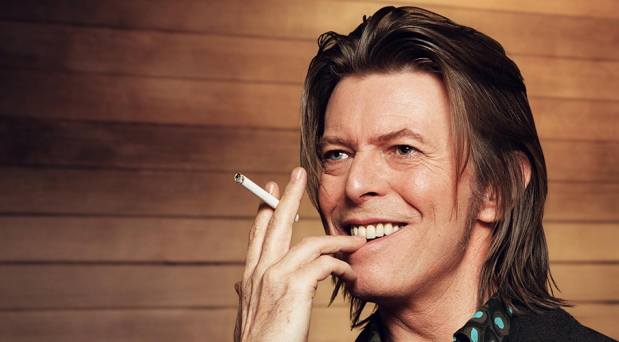An image of David Bowie smiling with a cigarette in his hand.